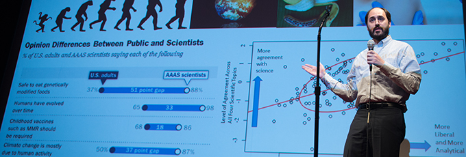 male presenting thesis in front of projected screen on stage